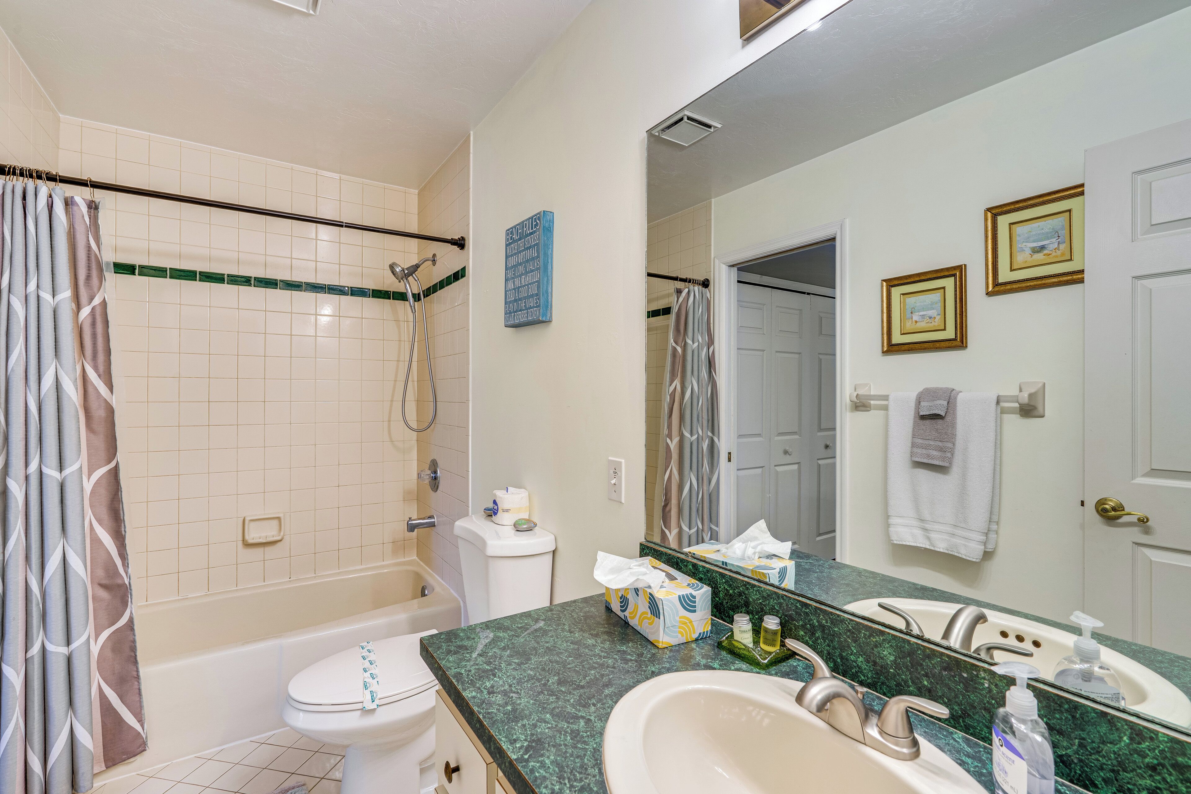 A bathroom with a bathtub, toilet, and sink. There is a shower curtain, a towel rack, and a mirror.