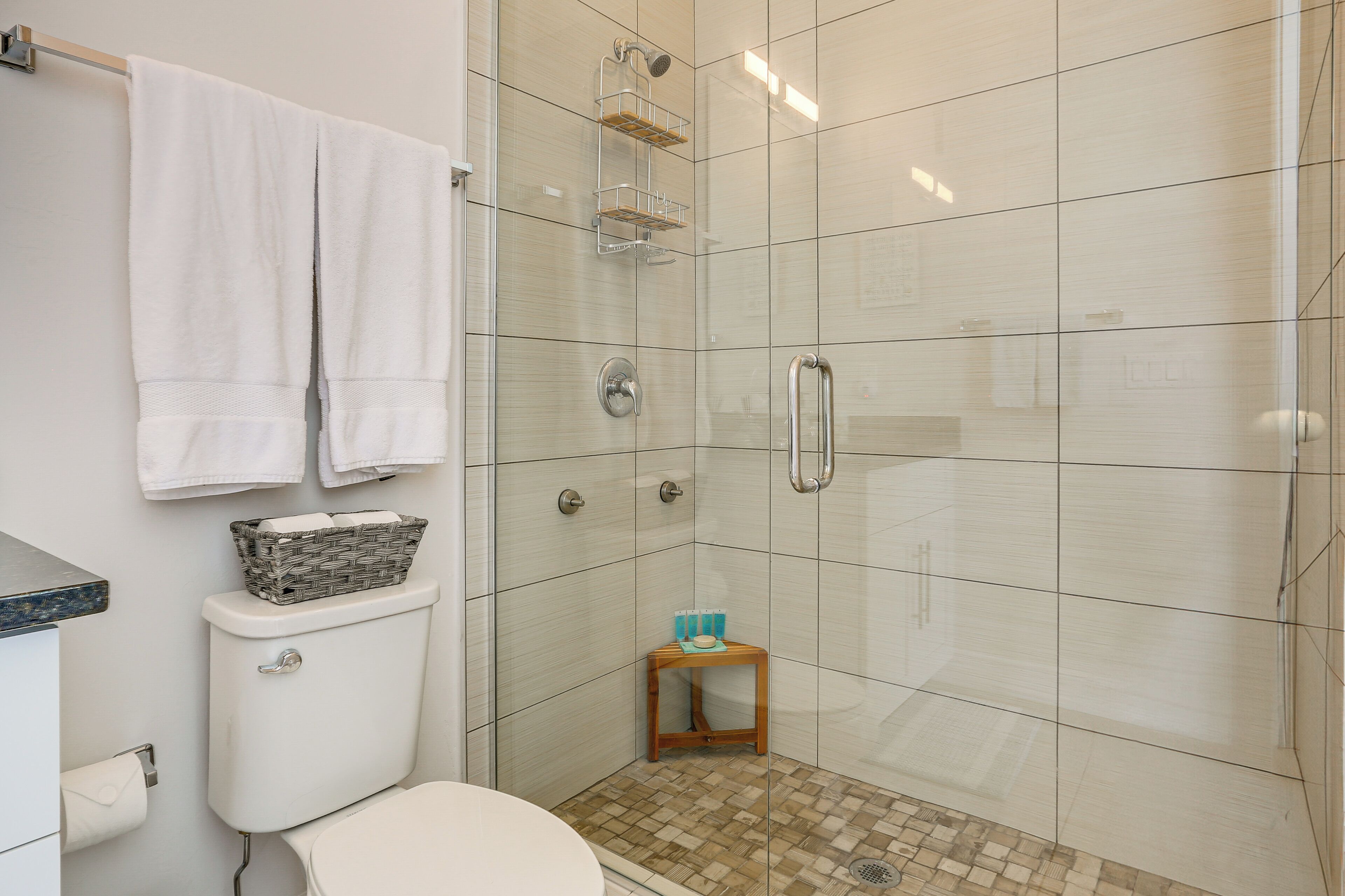 A modern bathroom with a glass shower enclosure, a toilet, and a small wooden stool.