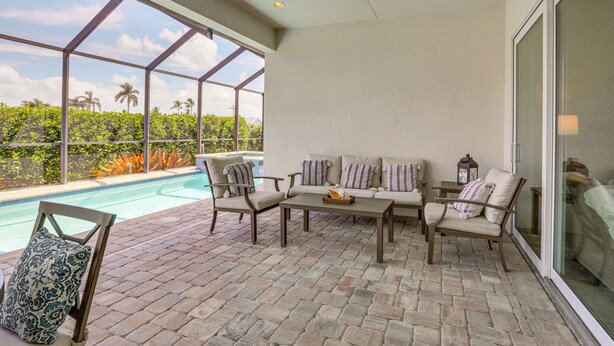 Un patio techado con piscina, mobiliario exterior y vista a palmeras.