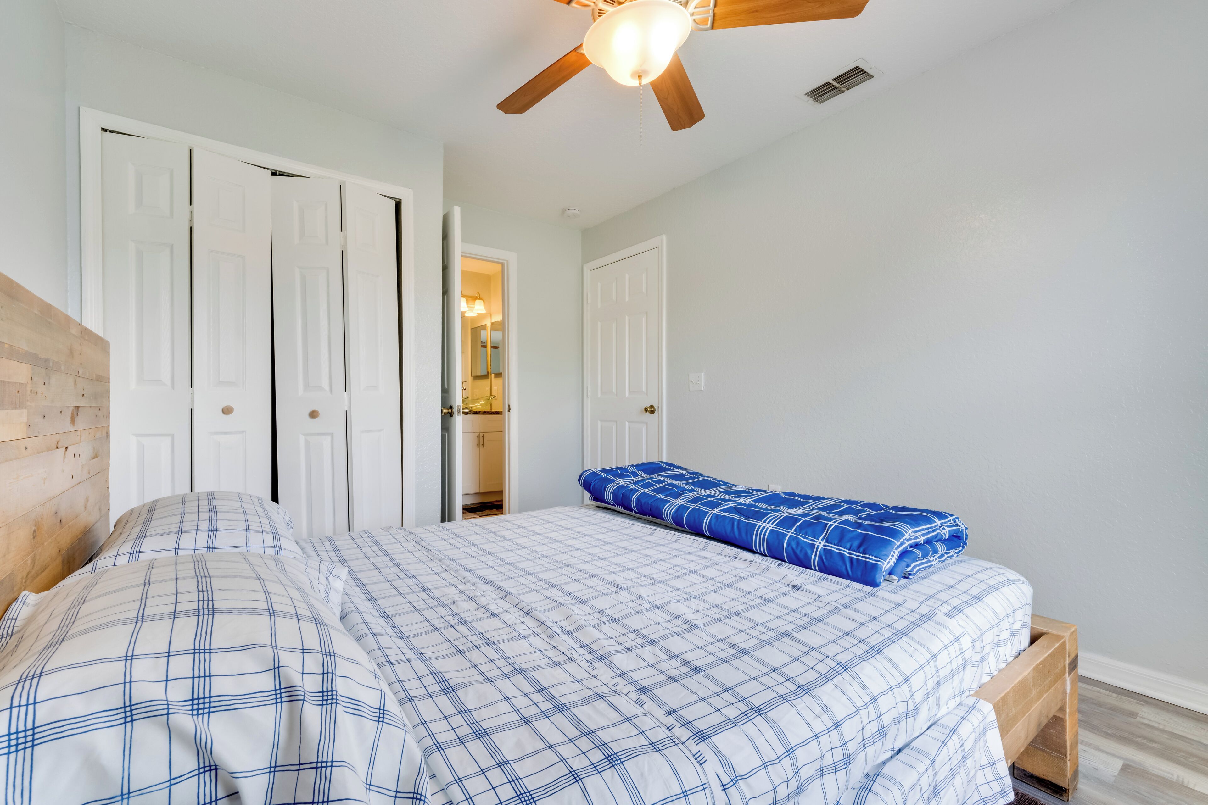 Quarto com uma cama, cabeceira de madeira, ventilador de teto e portas brancas.