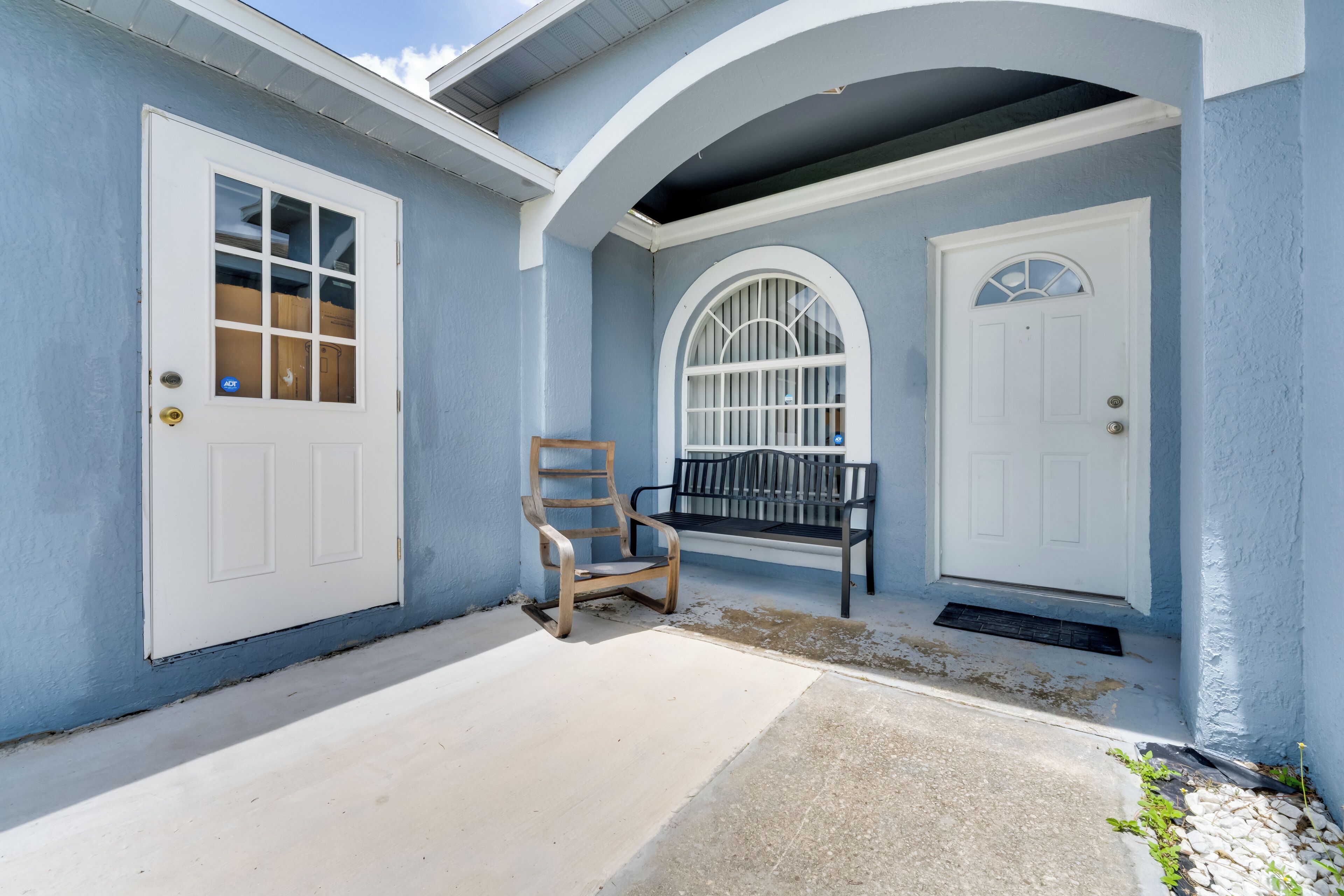 A house with two white doors, a wooden bench, and a small porch area.