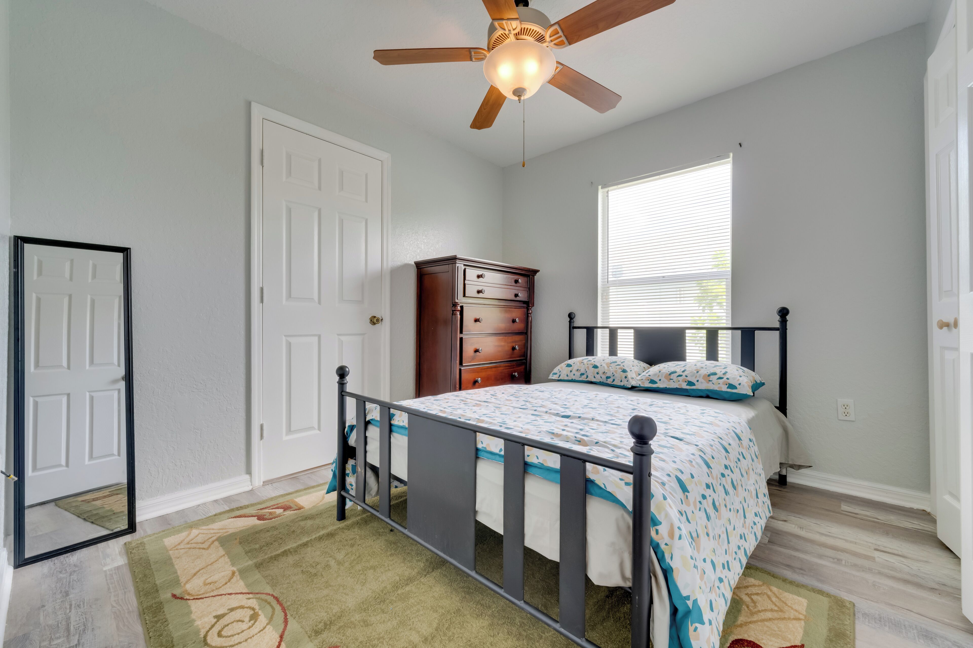 A bedroom with a bed, a dresser, a ceiling fan, and a window.