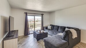 A modern living room with a grey sofa, a small ottoman, a flat-screen TV, and a sliding glass door leading to a balcony. - Lake Views & Boat Parking: Condo in Heart of LHC (Lake Havasu City)