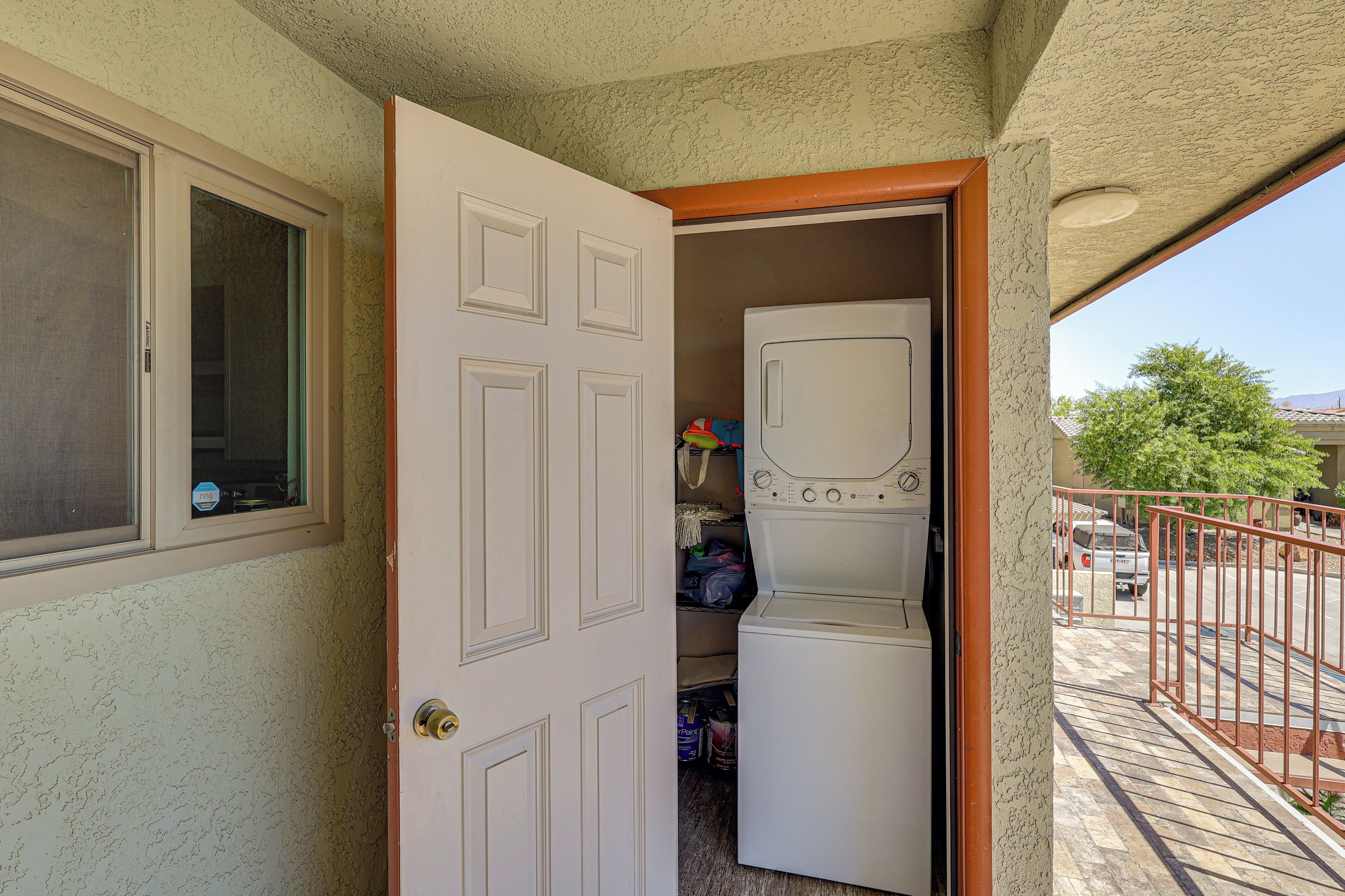 A laundry room with a washer and dryer, a door leading to a balcony, and a window with a view of the outside.