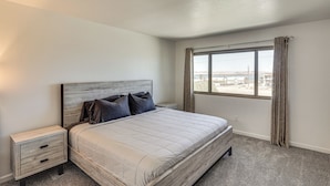 A bedroom with a large bed, a nightstand, a window with curtains, and a view of the city. - Lake Views & Boat Parking: Condo in Heart of LHC (Lake Havasu City)