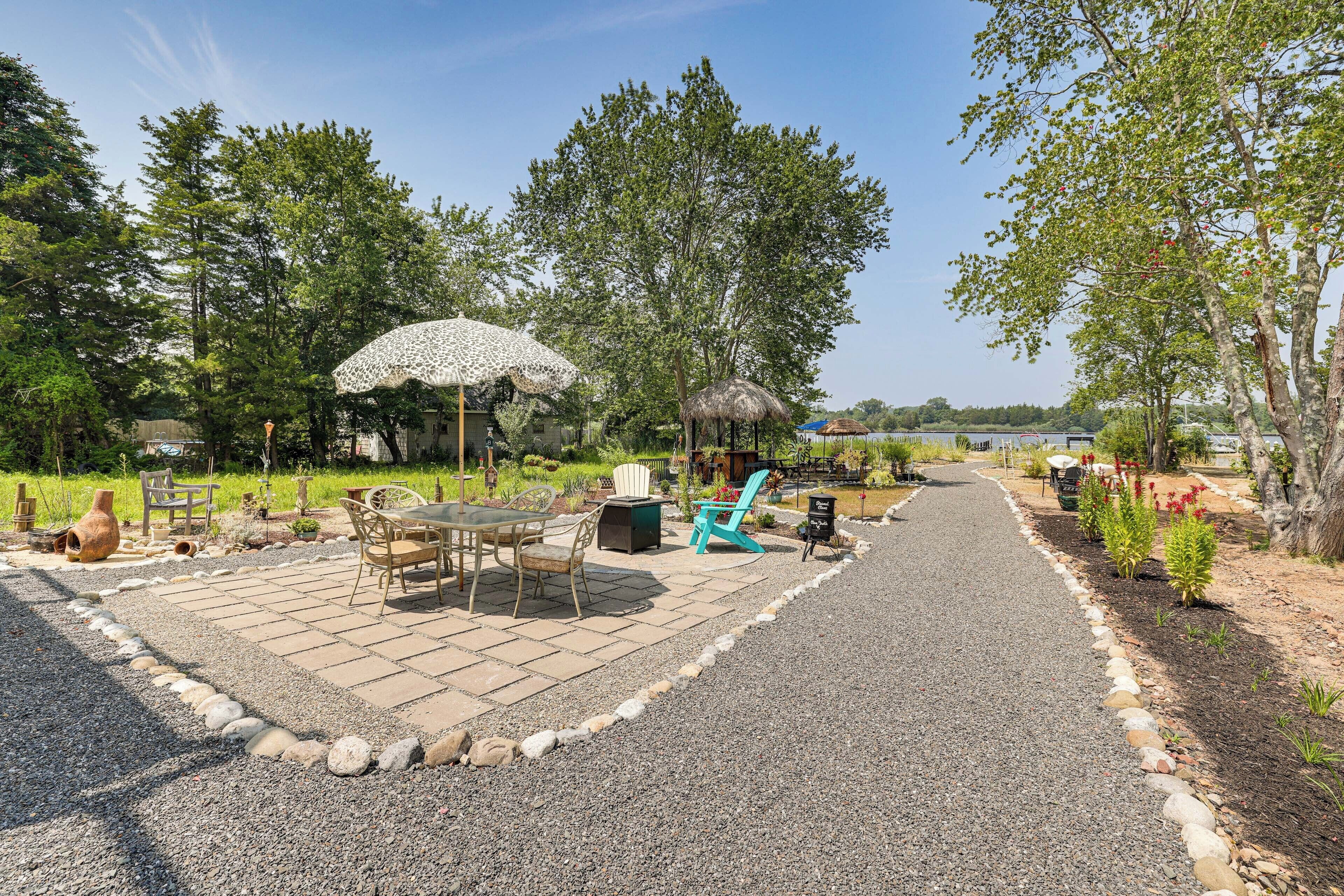 Un'area patio con tavolo e sedie, una struttura a tetto di paglia e un vialetto in ghiaia.