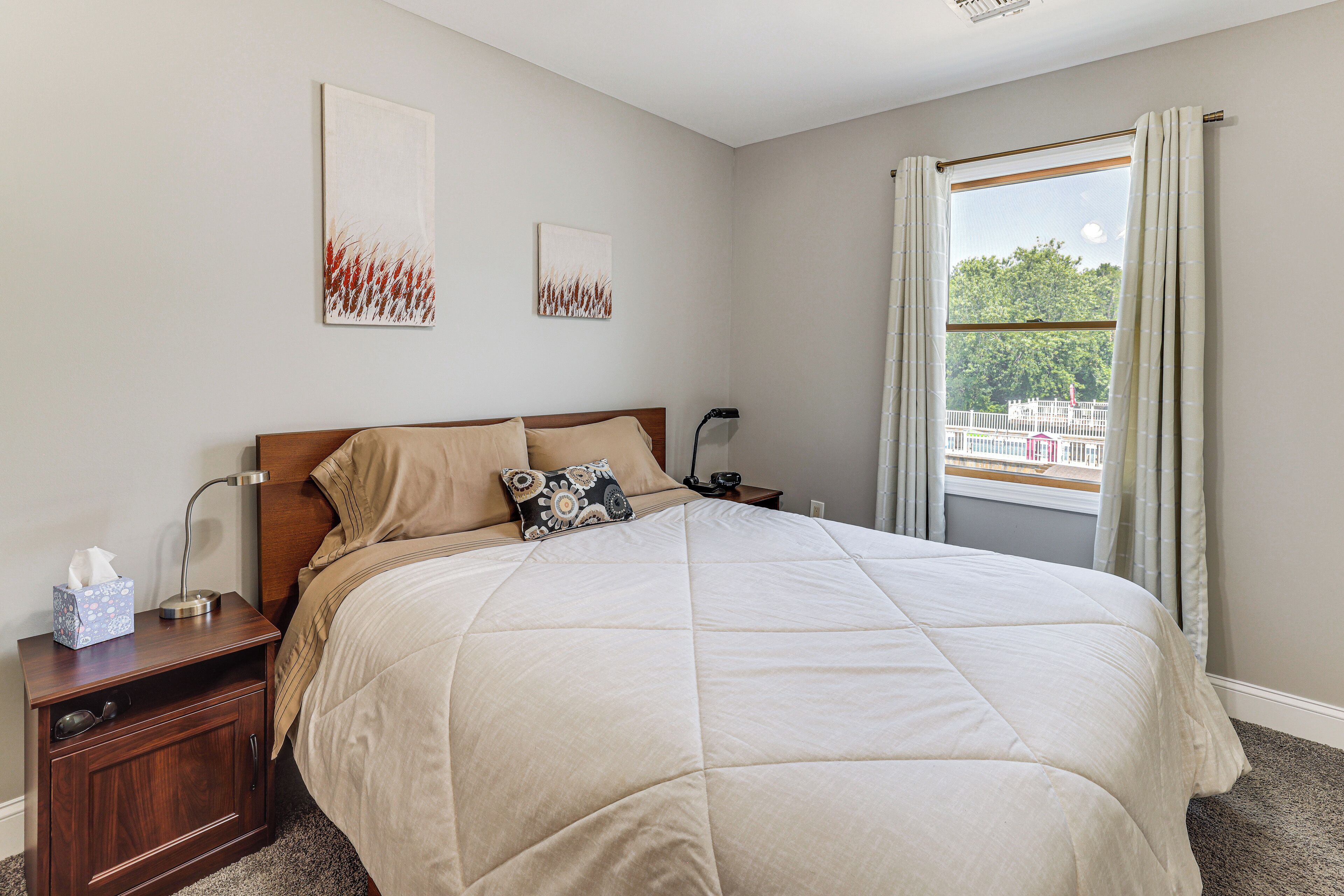 A neatly made bed with a beige comforter, a wooden headboard, and two wall-mounted artworks.