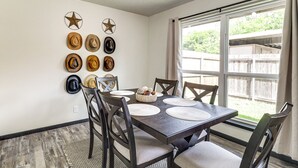 A dining area with a dark wooden table set for four, surrounded by dark wooden chairs with cushioned seats. The wall behind the table features a collection of hats and two star decorations. - 5 Mi to At&t Stadium: Townhome w/ Patio (Arlington)