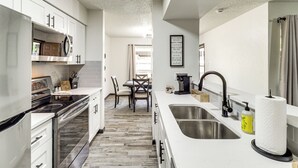A modern kitchen with white cabinets, stainless steel appliances, and a dining area with a table and chairs. - 5 Mi to At&t Stadium: Townhome w/ Patio (Arlington)