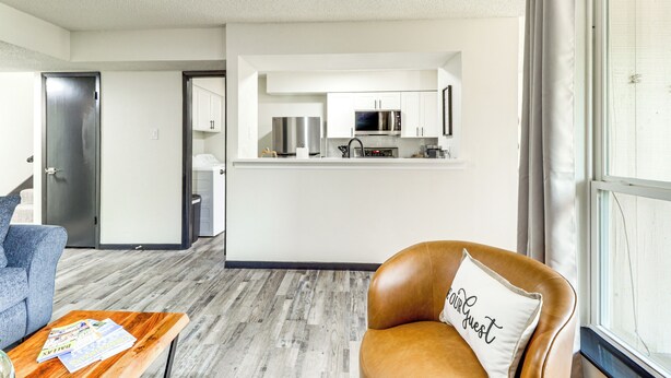 A modern living room with a brown leather chair, a wooden coffee table, and a view of a kitchen area with white cabinets and stainless steel appliances. - 5 Mi to At&t Stadium: Townhome w/ Patio (Arlington)