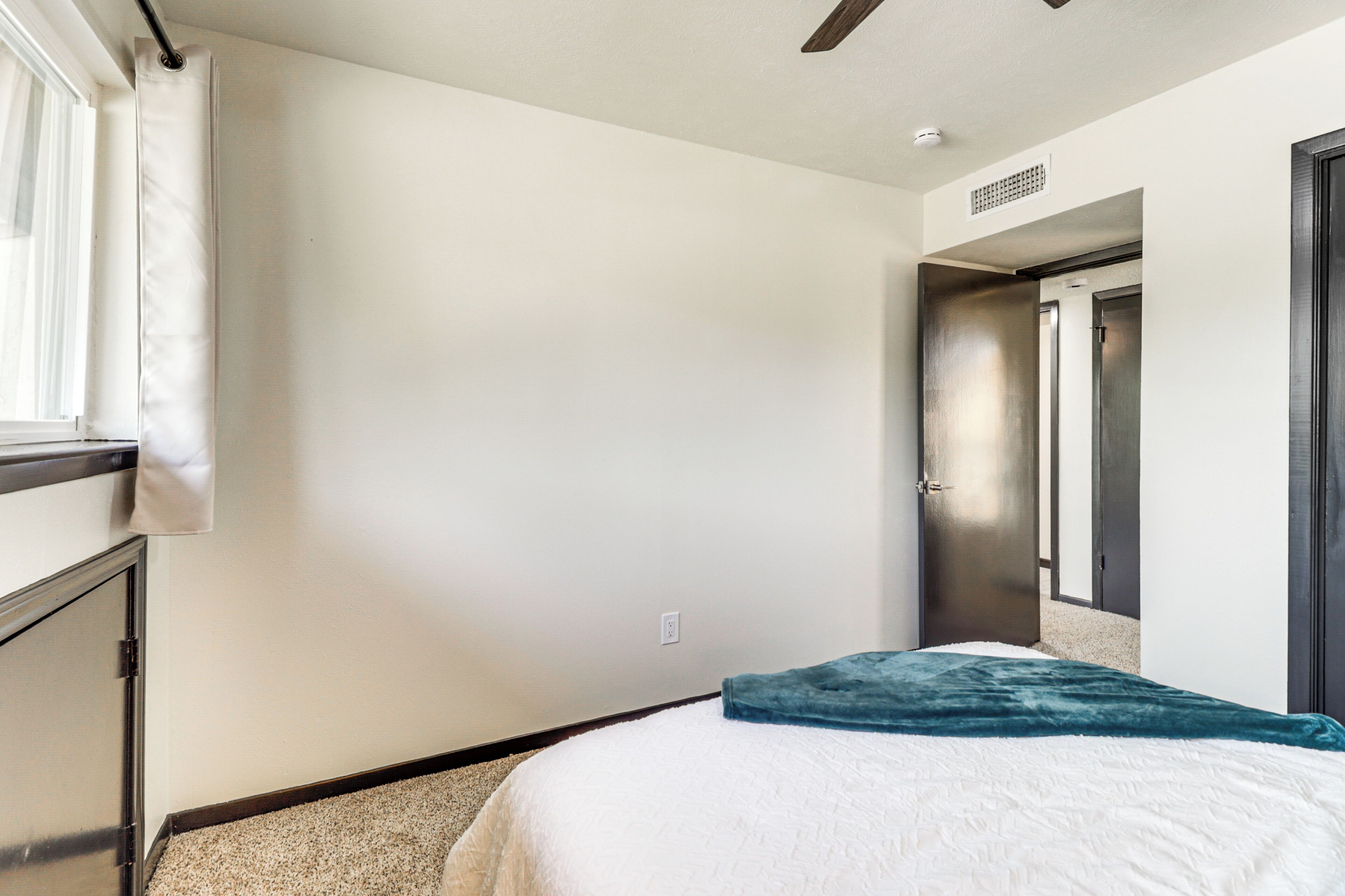 Une chambre d’hôtel avec un lit, une fenêtre avec des rideaux, une porte et un couloir menant à une autre chambre.