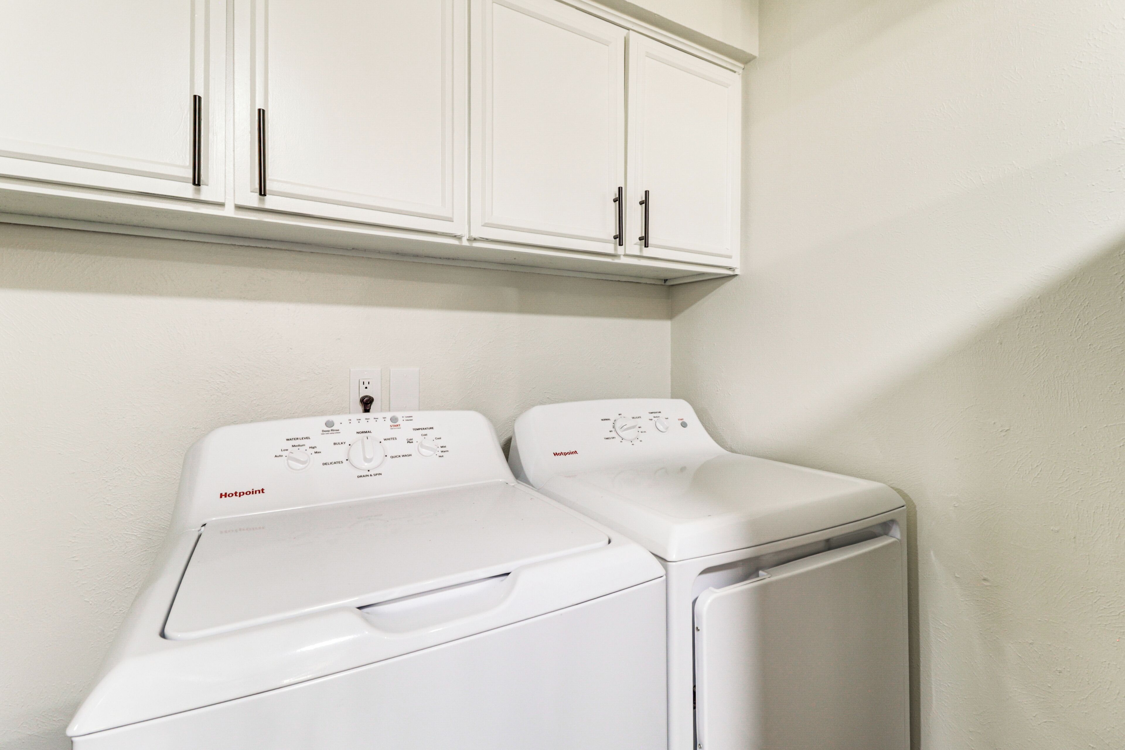 A laundry area with two white front-loading washing machines and a white cabinet above them.