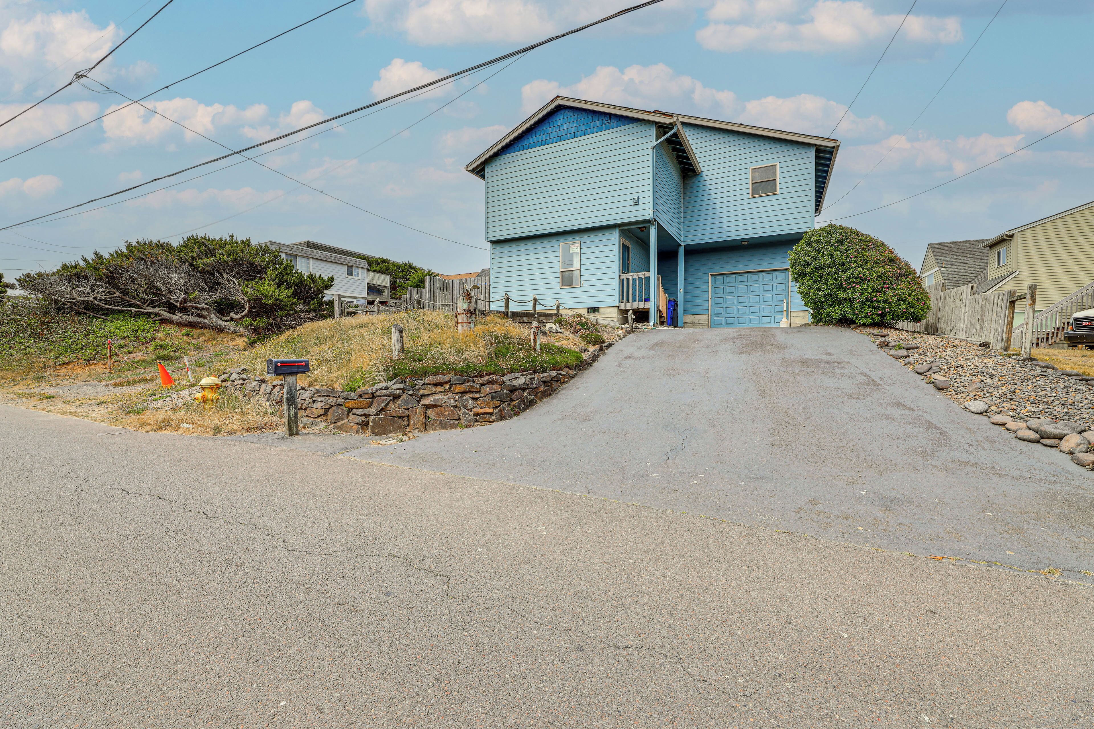 A two-story house with a blue exterior, a driveway leading to the front door, and a stone retaining wall on the left.