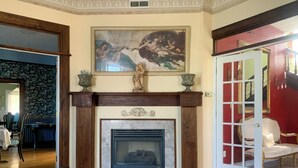 Une vaste pièce dotée d’une cheminée en marbre, d’un grand tableau classique accroché au-dessus et d’une porte rouge encadrée de blanc.