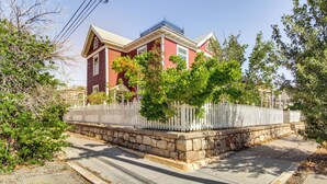 Une maison rouge avec une clôture blanche en bois, un soubassement en pierre et un ciel dégagé.