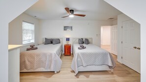 A bedroom with two beds, a ceiling fan, a small table with a lamp, and a door.