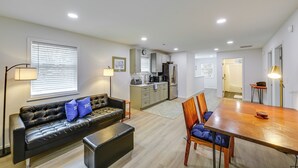 A modern living room with a sofa, a dining table, and a kitchen in the background.