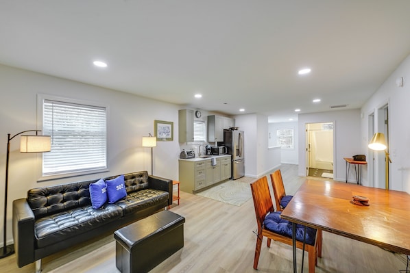 A modern living room with a sofa, a dining table, and a kitchen in the background. - 4 Mi to Rehoboth Beach: Cozy Coastal Apt! (Rehoboth Beach)