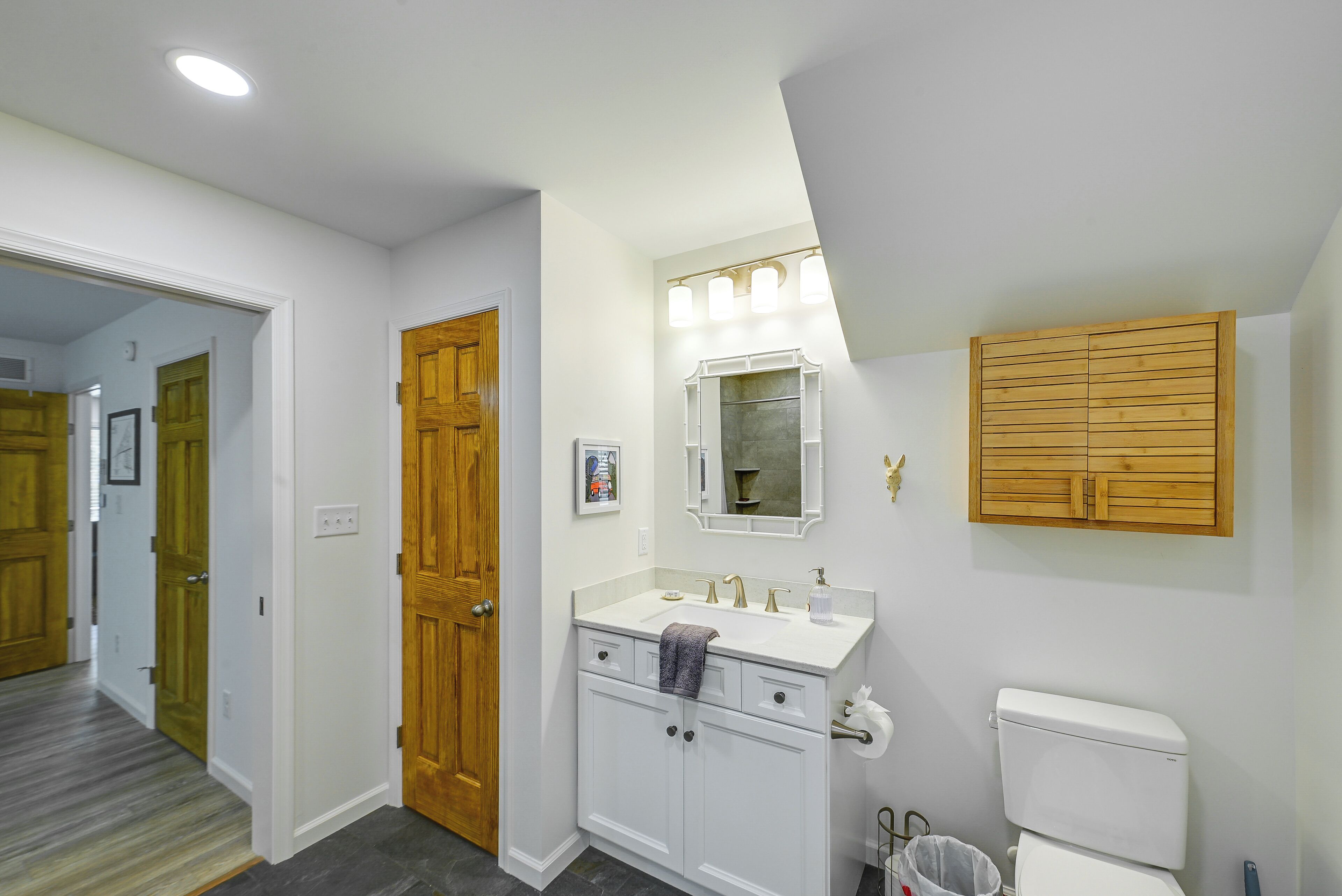 Un baño con un tocador blanco, un armario de madera, un espejo con luces y un inodoro.