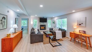 Un salon moderne avec une cheminée, deux canapés, une table basse et un bureau avec des chaises.