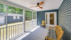 Une véranda couverte avec un ventilateur de plafond, une chaise en osier et une vue sur la maison voisine.