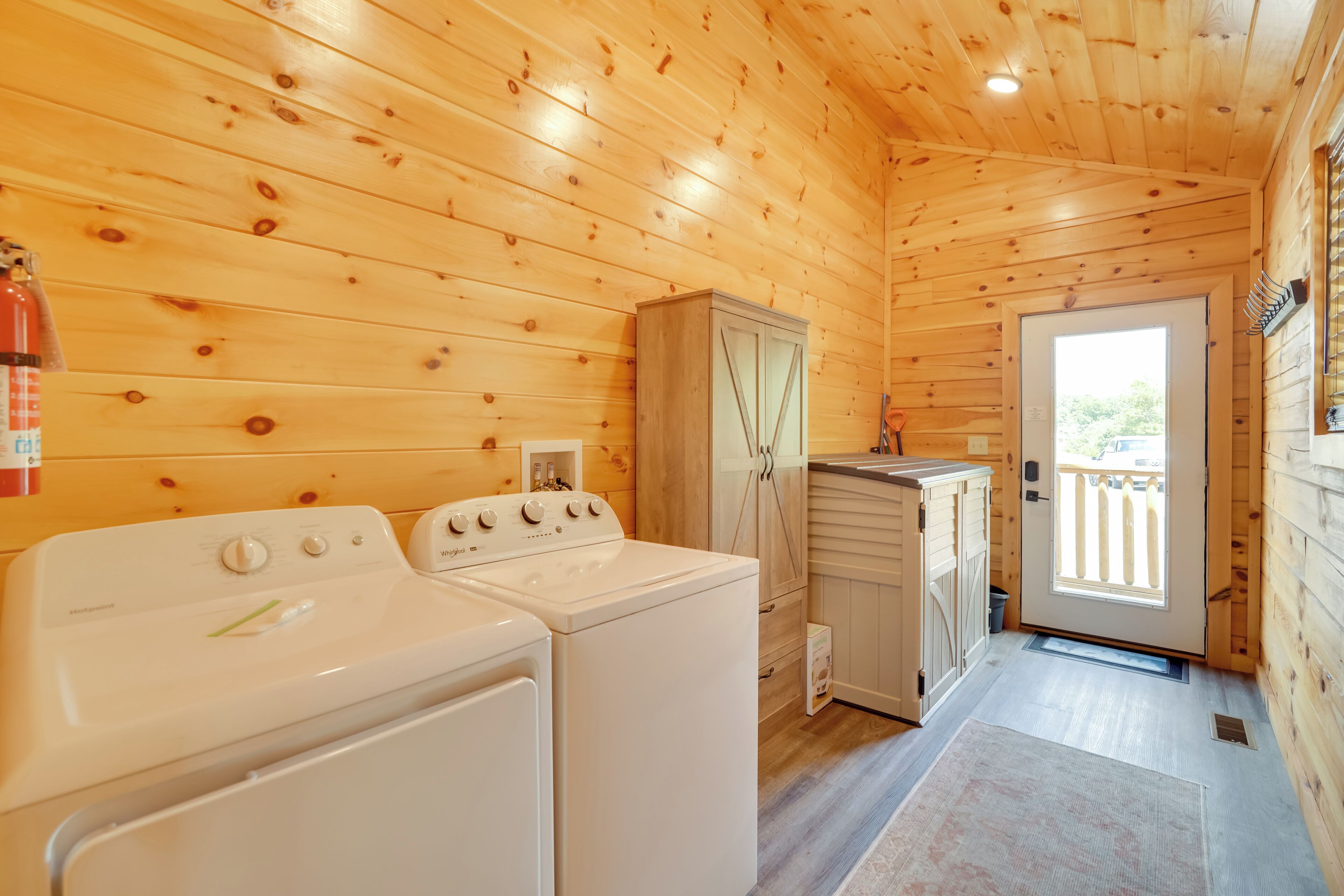 A wooden cabin interior with a washing machine, a cabinet, and a door leading outside.