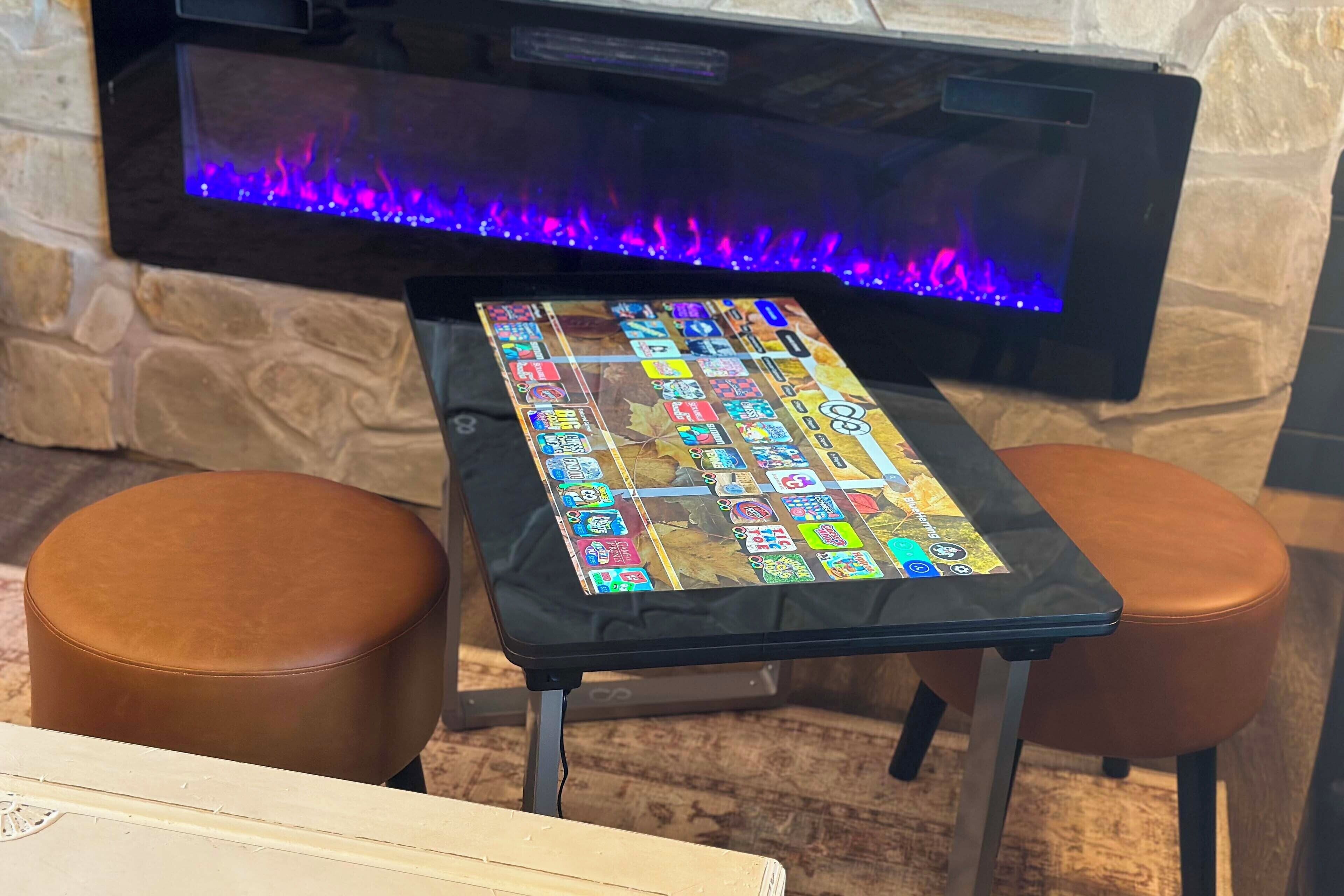 Une table sur laquelle est posé un jeu de société aux couleurs vives, devant une cheminée où brûle un feu aux flammes bleues.