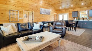 A cozy log cabin interior with a leather sofa, a dining table, and a kitchen area.