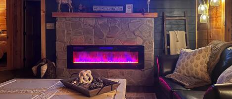 L’intérieur d’un chalet accueillant, avec une cheminée en pierre, un téléviseur fixé au-dessus et un canapé en cuir.