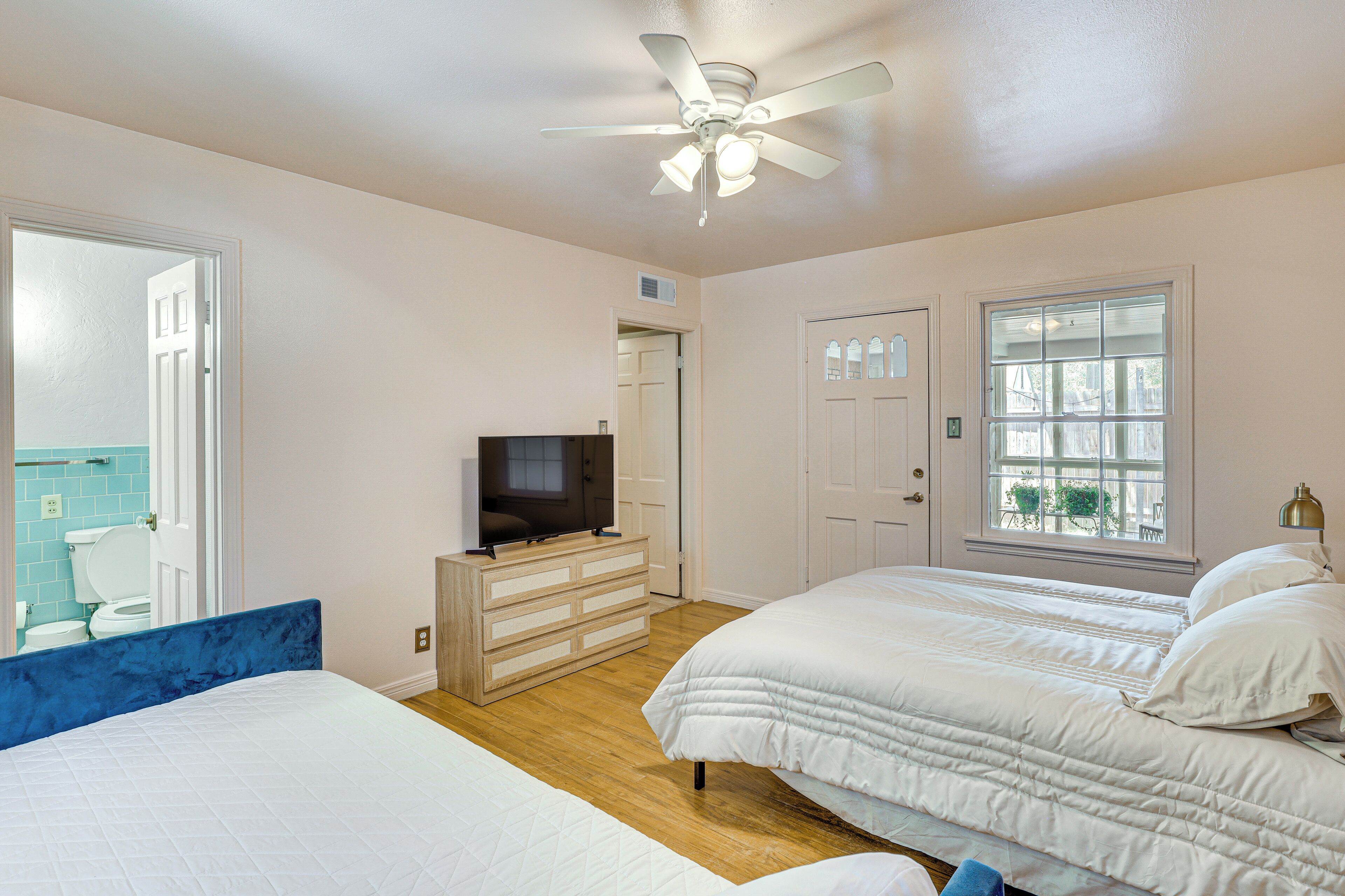 A bedroom with two beds, a ceiling fan, a TV, and a window with a view.