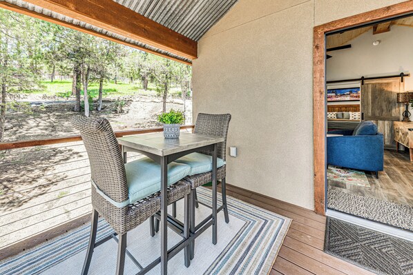 A covered patio with a table and chairs, a view of the outdoors, and a door leading to an interior space with a sofa.