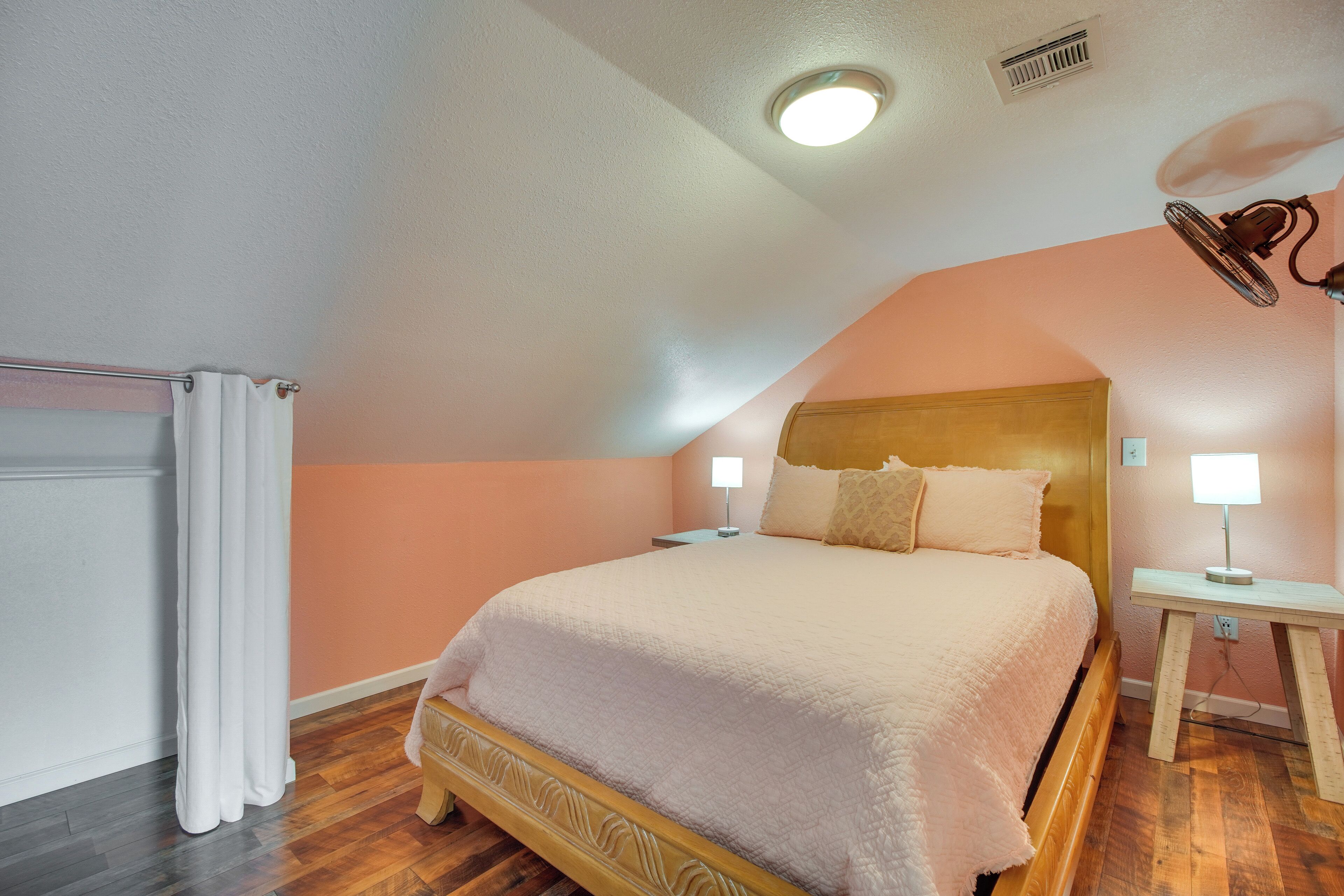 A bedroom with a bed, bedside lamps, a ceiling fan, and a nightstand.