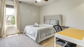 Une chambre à coucher avec un lit, un ventilateur de plafond, une fenêtre avec des rideaux et une petite table avec une chaise.