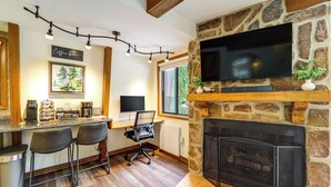 A cozy living area with a stone fireplace, a flat-screen TV mounted on the wall, and a coffee bar with stools and a coffee machine.