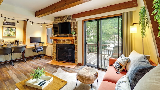 A cozy living room with a stone fireplace, a comfortable sofa, a dining area with a bar, and a large sliding glass door leading to a deck.