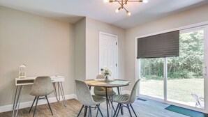 Un coin repas avec une table ronde, quatre chaises, un bureau blanc et une grande fenêtre donnant sur l’extérieur.
