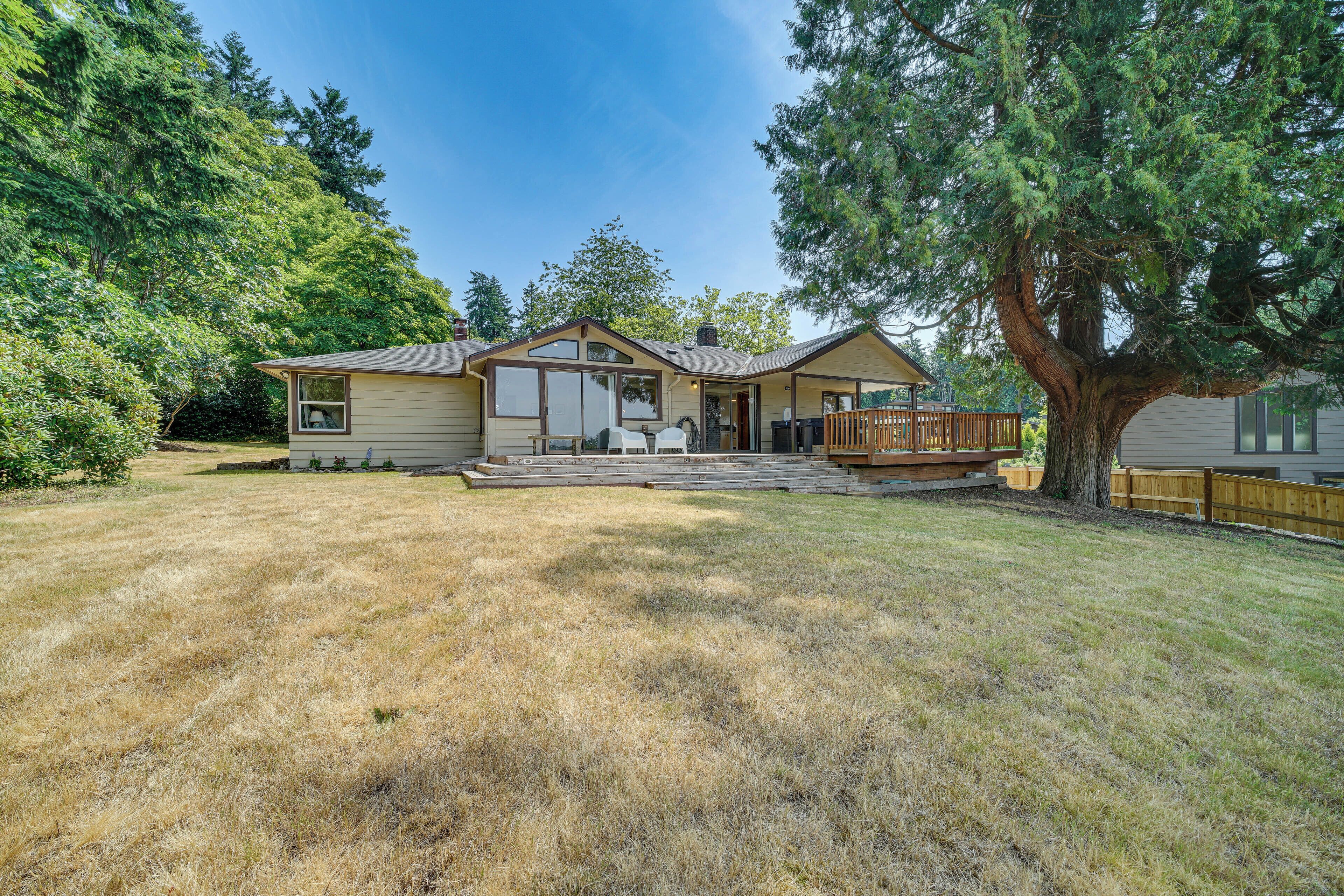 A single-story house with a front porch, a covered patio, and a large tree in the yard.