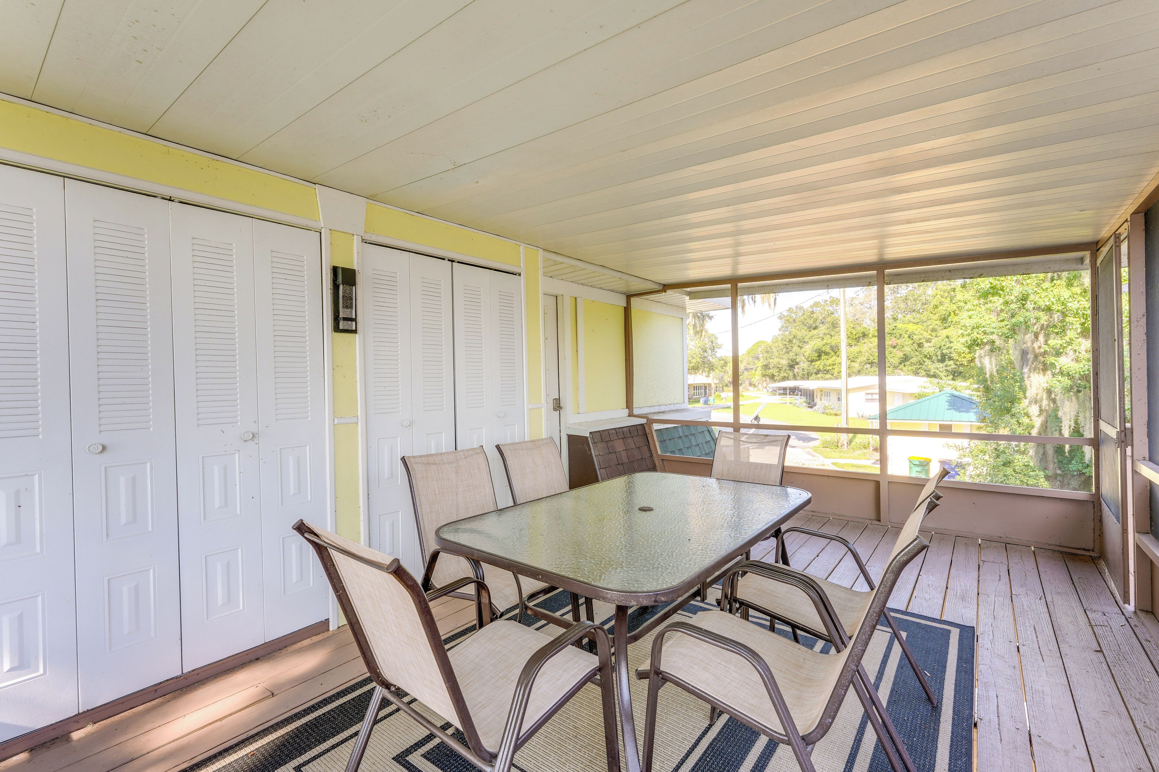 Une véranda abritée avec une table et des chaises, une vue sur l’extérieur et une rangée de portes blanches.