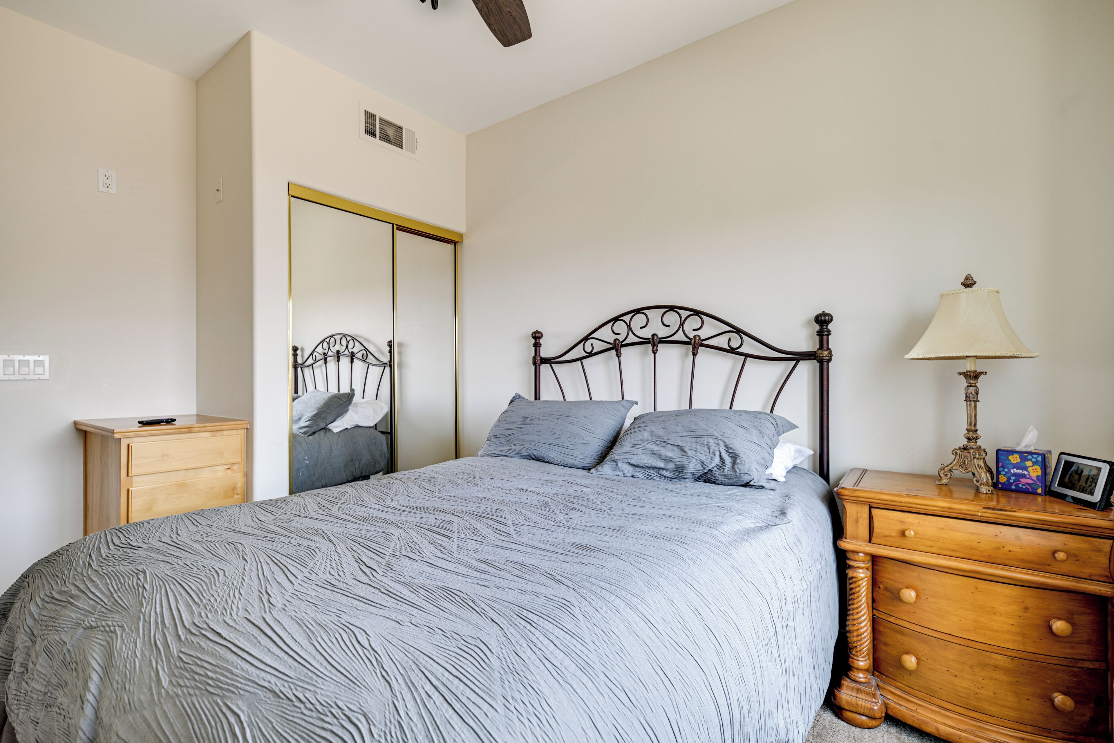 A bedroom with a bed, a wooden nightstand, a dresser, a mirror, and a ceiling fan.