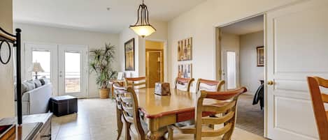 A dining area with a wooden table and chairs, a hanging light fixture, and a potted plant.