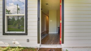 A house entrance with a wooden door, a window with blinds, and a visible hallway leading inside.