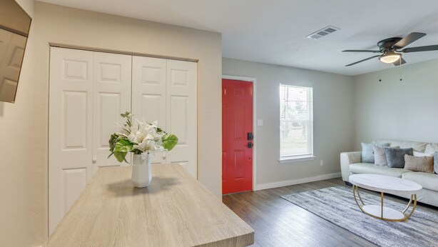 A living room with a wooden coffee table, a red door, a white sofa, and a ceiling fan.