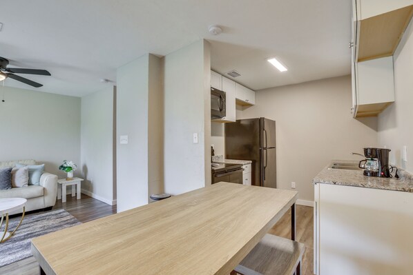 Une cuisine moderne avec une table en bois, des appareils en acier inoxydable et un plan de travail blanc.