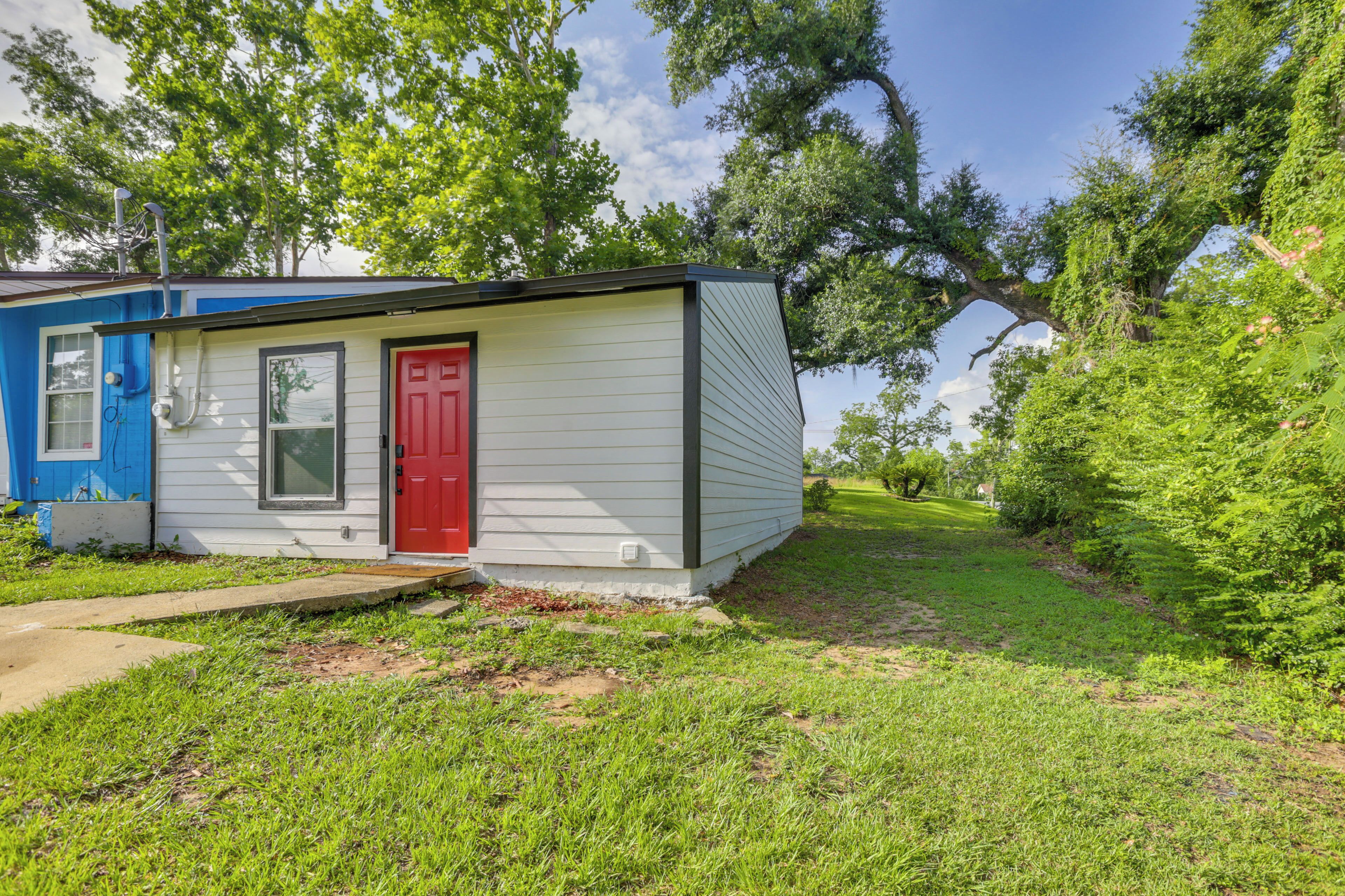 A small, single-story house with a red door, surrounded by a grassy yard and trees.