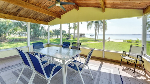 A covered patio with a table and chairs, large windows with a view of the ocean, and a ceiling fan. - Lake Dora Escape: Canal Access & Seaplane Sights! (Tavares)