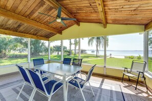 Un patio cubierto con mesa y sillas, ventanas amplias con vista al océano y un ventilador de techo.