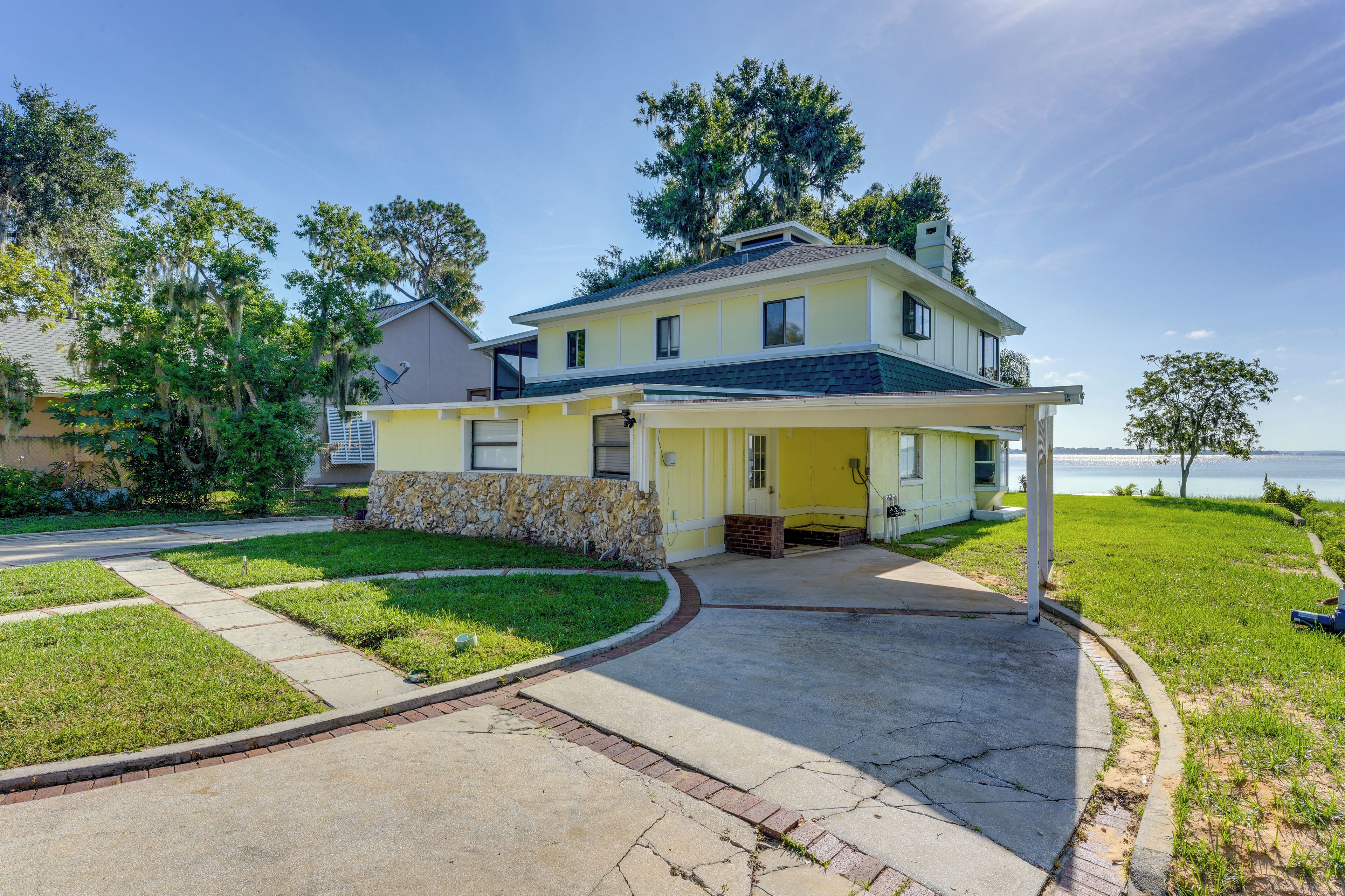 A two-story house with a covered porch, a stone foundation, and a view of the water.