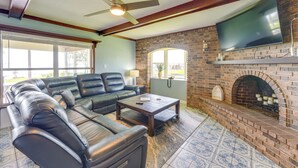 A living room with a brick fireplace, leather sofa, and a flat-screen TV mounted on the wall. - Lake Dora Escape: Canal Access & Seaplane Sights! (Tavares)