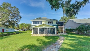 A two-story house with a large glass enclosure, a stone pathway, and a well-maintained lawn. - Lake Dora Escape: Canal Access & Seaplane Sights! (Tavares)