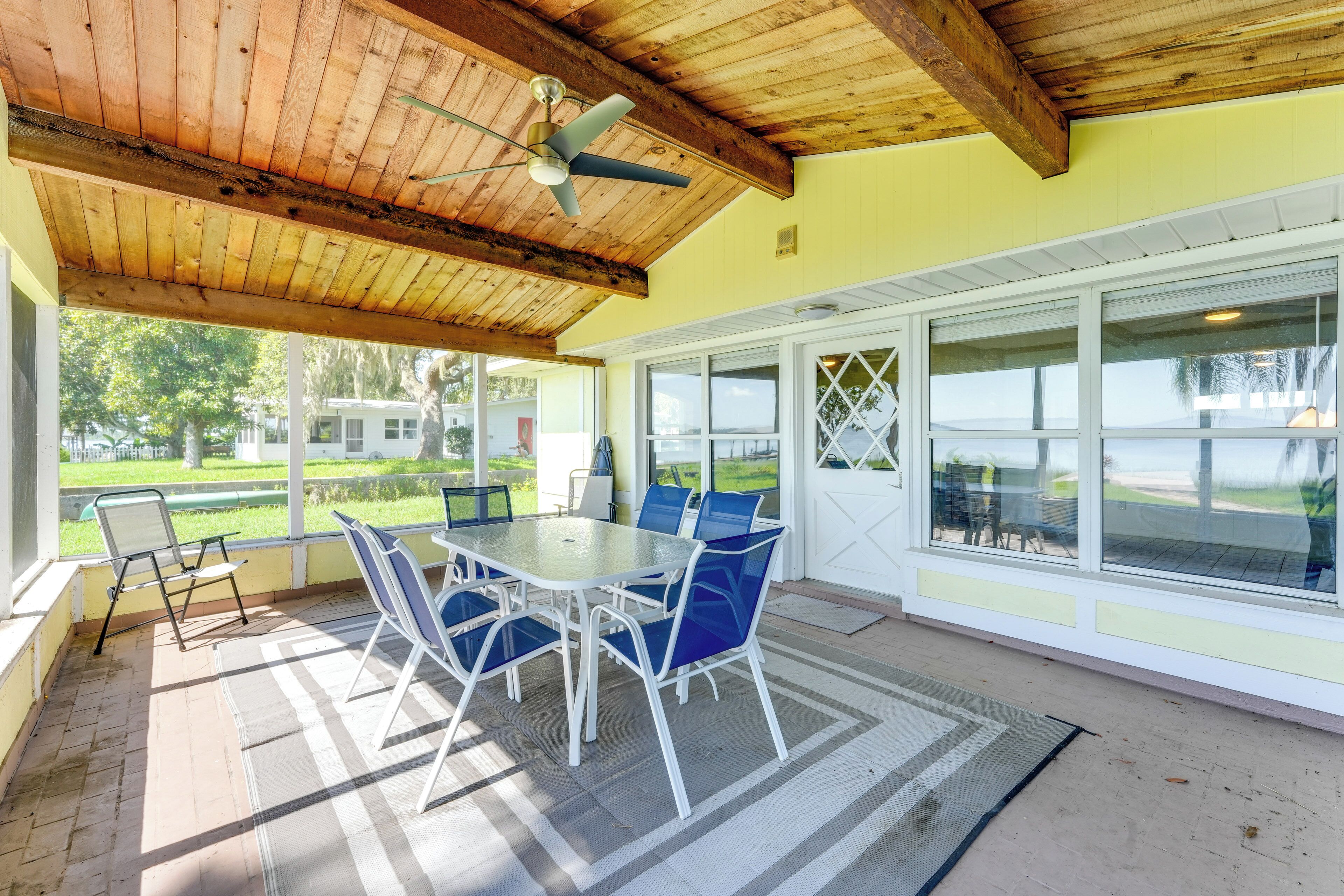 Une terrasse couverte avec une table et des chaises, de grandes fenêtres et un ventilateur de plafond.